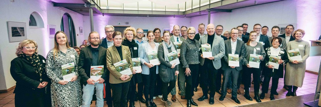 Gruppenfoto von circa 30 Menschen. Alle halten eine Broschüre in der Hand.