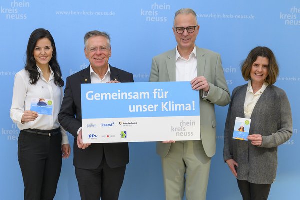 Landrat Hans-Jürgen Petrauschke (2.v.l.) mit Kreisdirektor Dirk Brügge und den Klimaschutzmanagerinnen Ina Grothe (l.) und Regina Krings vor einer blauen Wand mit Rhein-Kreis Neuss Logo. Die beiden Herren in der Mitte halten ein Schild mit der Aufschrift "Gemeinsam für unser Klima" hoch.