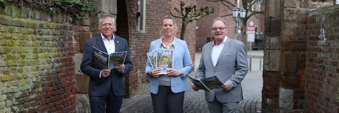 Zwei Männer und eine Frau it einer Broschüre in der Hand.