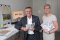 Landrat Hans-Jürgen Petrauschke und Claudia Trampen halten jeweils einsn Flyer