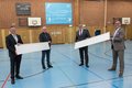 Landrat Hans-Jürgen Petrauschke, Michael Schlesiger, Edelbert Jansen und Harald Vieten halten zwei LED-Paneele in einer Sporthalle