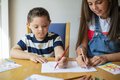 Ein kleiner Junge und ein etwas größeres Mädchen sitzen an einem tisch und zeichnen gemeinsam auf einem Blatt Papier.
