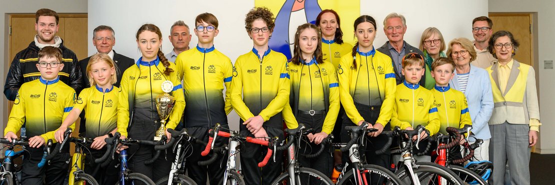 Rasportjugendmannschaft in gelben Trikots mit Fahrrädern auf Gruppenfoto u.a. mit Landrat Hans-Jürgen Petrauschke.