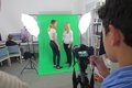 Eine männliche Person mit Kamera filmt zwei weibliche Personen vor einem grünen Hintergrund