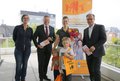 Hans-Jürgen Petrauschke, der Neusser Bürgermeister Reiner Breuer, Marion Klein und Sina Fabri mit ihren beiden Kindern vor einem Plaket der Familienkarte und halten ihre Gewinner in der Hand. Im Hintergrund ist die Stadt Neuss zu sehen.