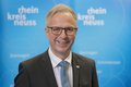 Kreisdirektor Dirk Brügge lächelnd vor blauer Fotowand mit Logos Rhein-Kreis Neuss