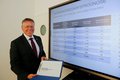 Landrat Hans-Jürgen Petrauschke halt Dokument in der Hand; vor Monitor mit Präsentation der Wohnungsbedarfsanalyse für den Rhein-Kreis Neuss 