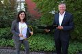 Landrat Hans-Jürgen Petrauschke und Marina Tressel stehen lächelnd vor einer grünen Hecke. Sie hält ein Glasfaserkabel in der Hand, er eine Dokumentenmappe